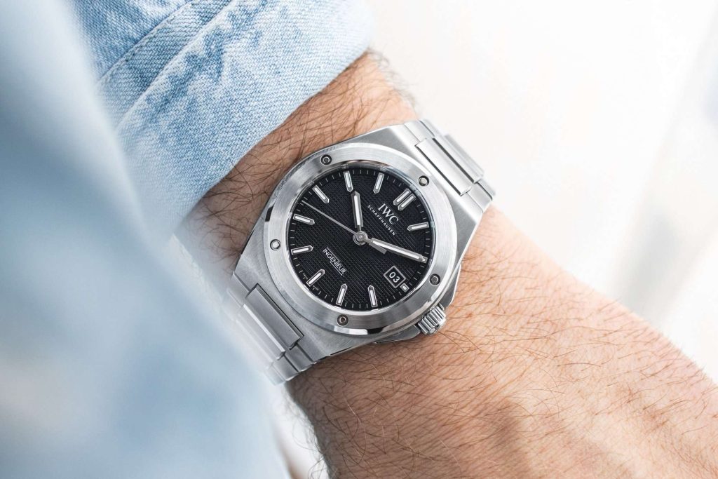 IWC Ingenieur mit schwarzem Zifferblatt abgebildet an einem Handgelenk mit hellblauem Ärmel vor weißem Hintergrund