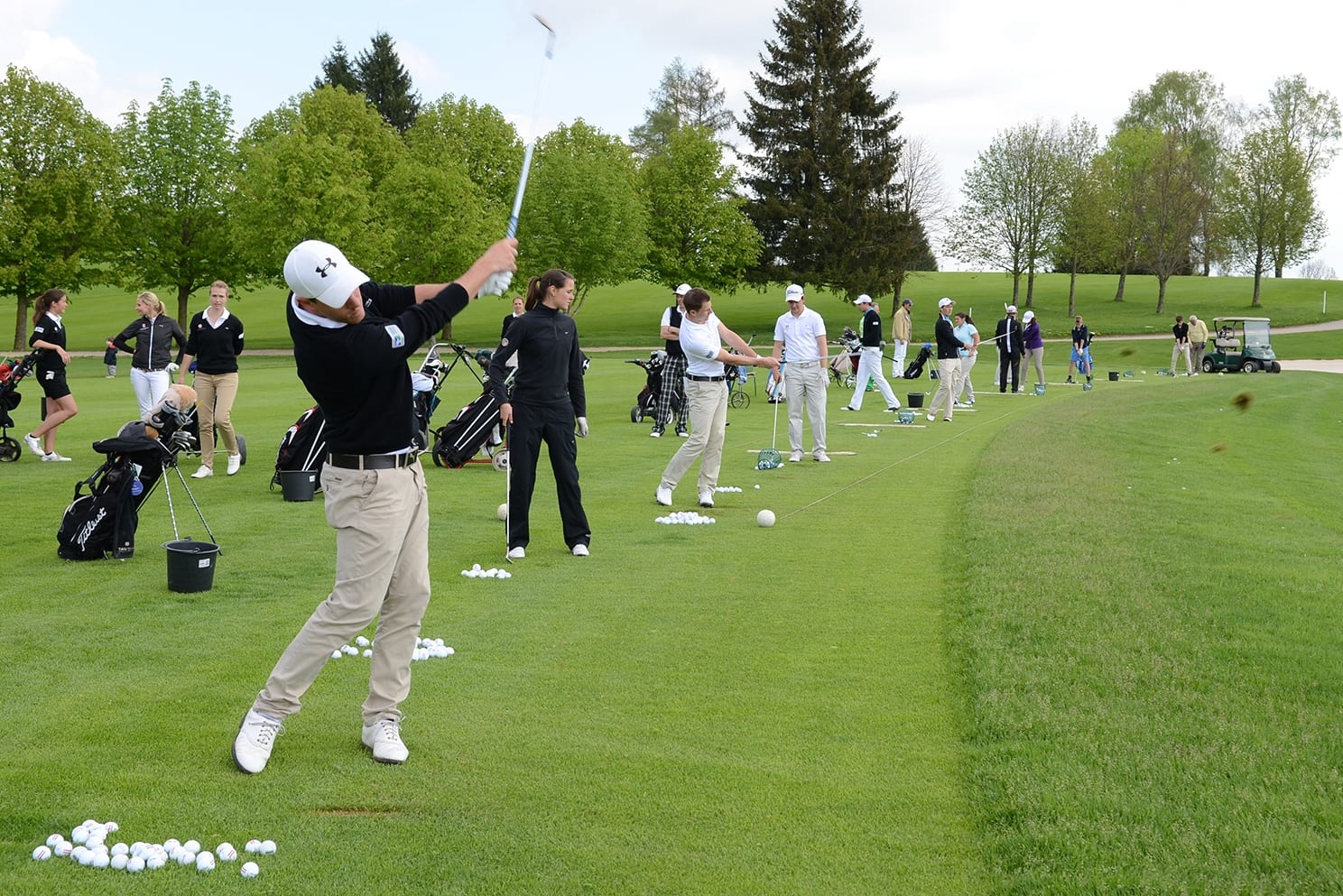 Zahlreiche Golfspielerinnen und Golfspieler mit Schlägern in der Hand auf dem Rasen des Münchener Golf Clubs