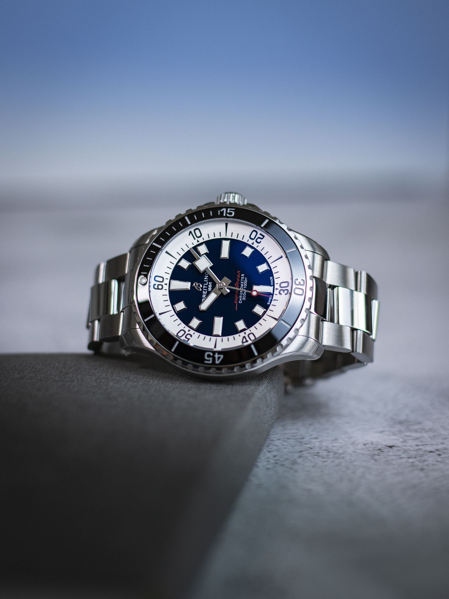 Breitling Superocean mit blauem Zifferblatt und schwarzer Lünette liegend vor grauem Hintergrund