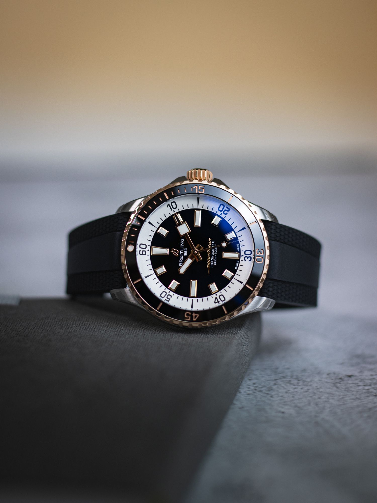 Breitling Superocean in schwarz mit goldenen Akzenten liegend vor grauem Hintergrund