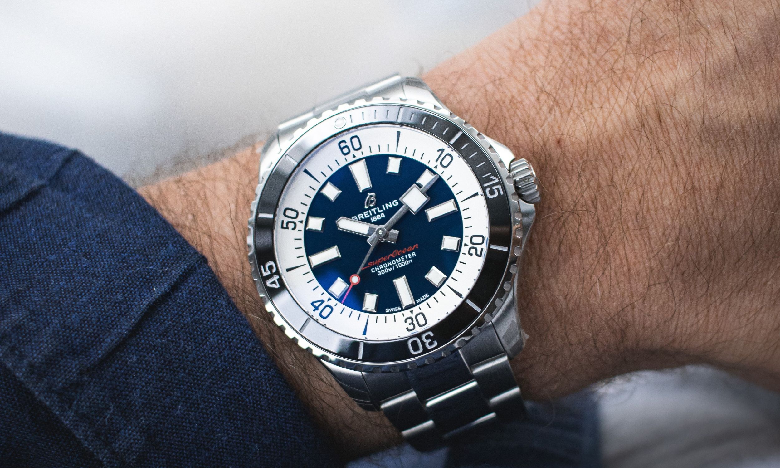 Die Breitling Superocean mit blauem Zifferblatt und schwarzer Lünette mit Edelstahlarmband abgebildet an einem Handgelenk vor hellem Hintergrund