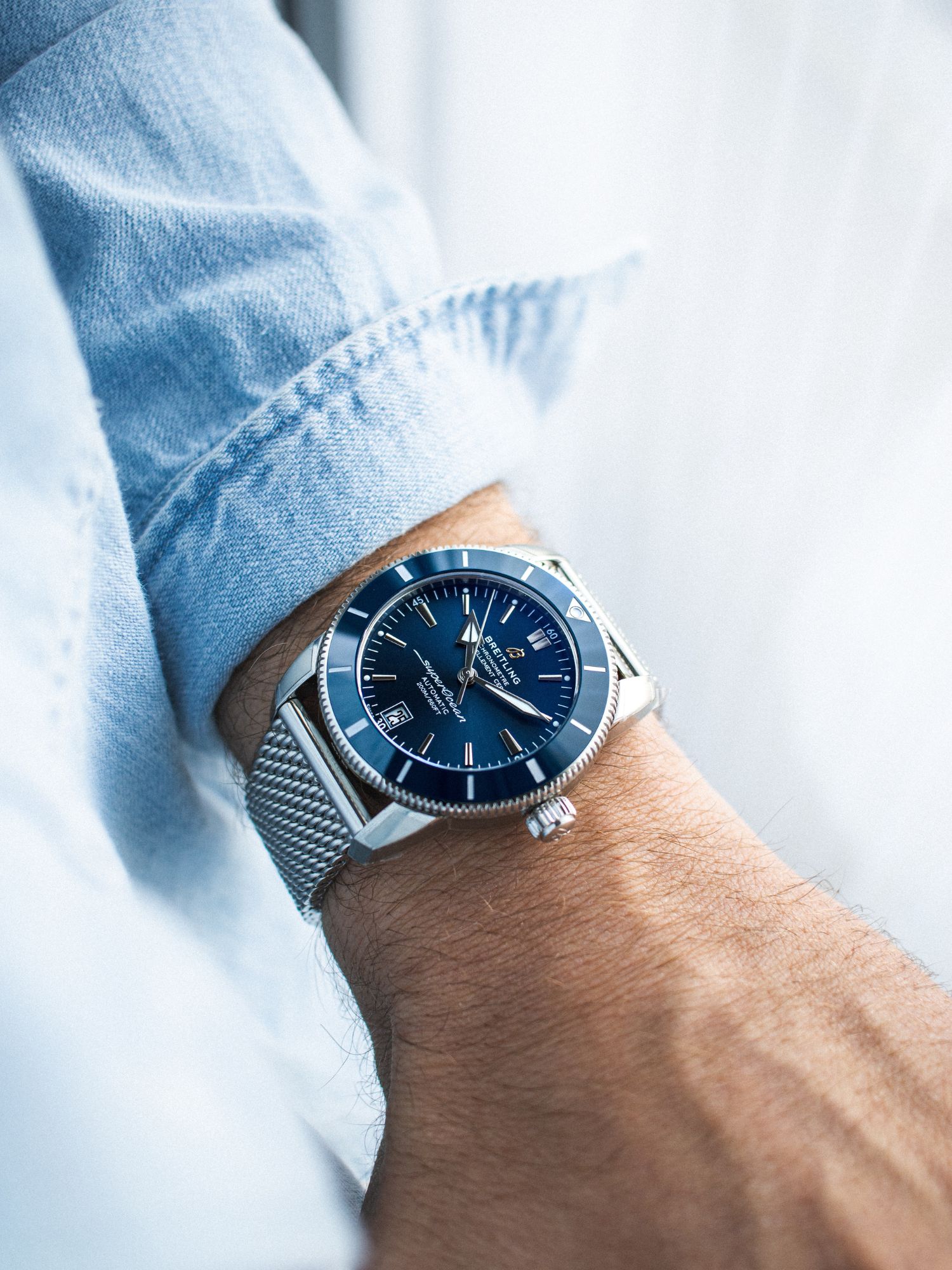 Breitling Superocean Heritage in blau am Handgelenk vor blauem Hintergrund