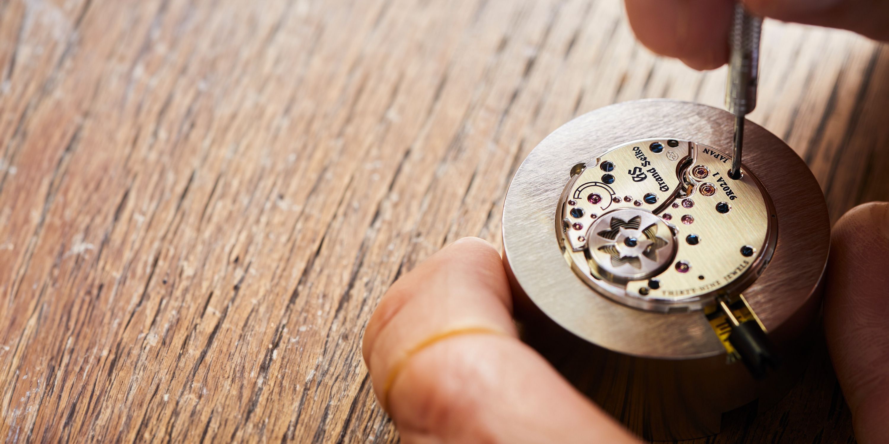 Das Kaliber 9R von Grand Seiko auf einem Holztisch liegend während der Montage eines Uhrmachers, dessen Hände zu sehen sind