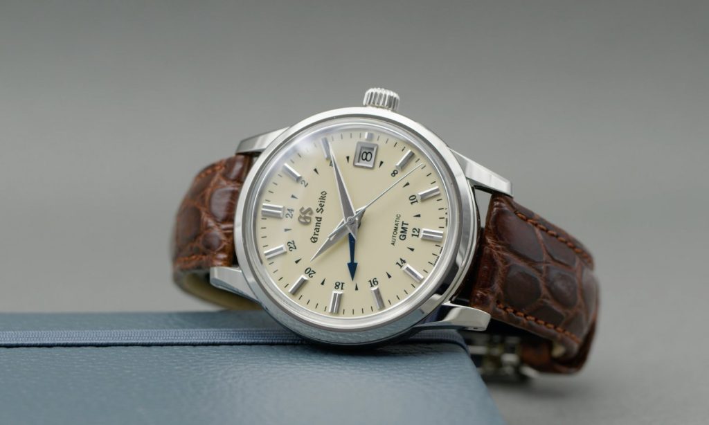 Grand Seiko Automatic GMT Referenz SBGM221 mit cremeweißem Zifferblatt am braunen Lederarmband auf der Seite liegend vor hellgrauem Hintergrund