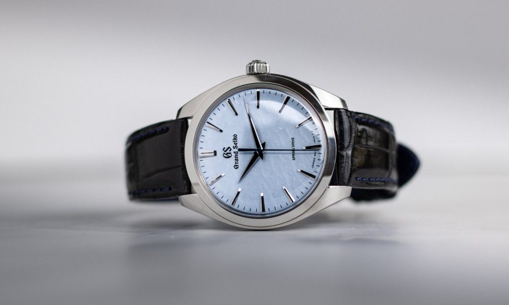 Grand Seiko Omiwatari Referenz SBGY007 mit hellblauem Zifferblatt am schwarzen Lederarmband auf der Seite liegend vor hellgrauem Hintergrund