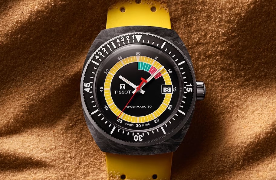 Tissot Sideral mit gelbem Zifferblatt und gelbem Armband liegend auf einem sandigen Untergrund