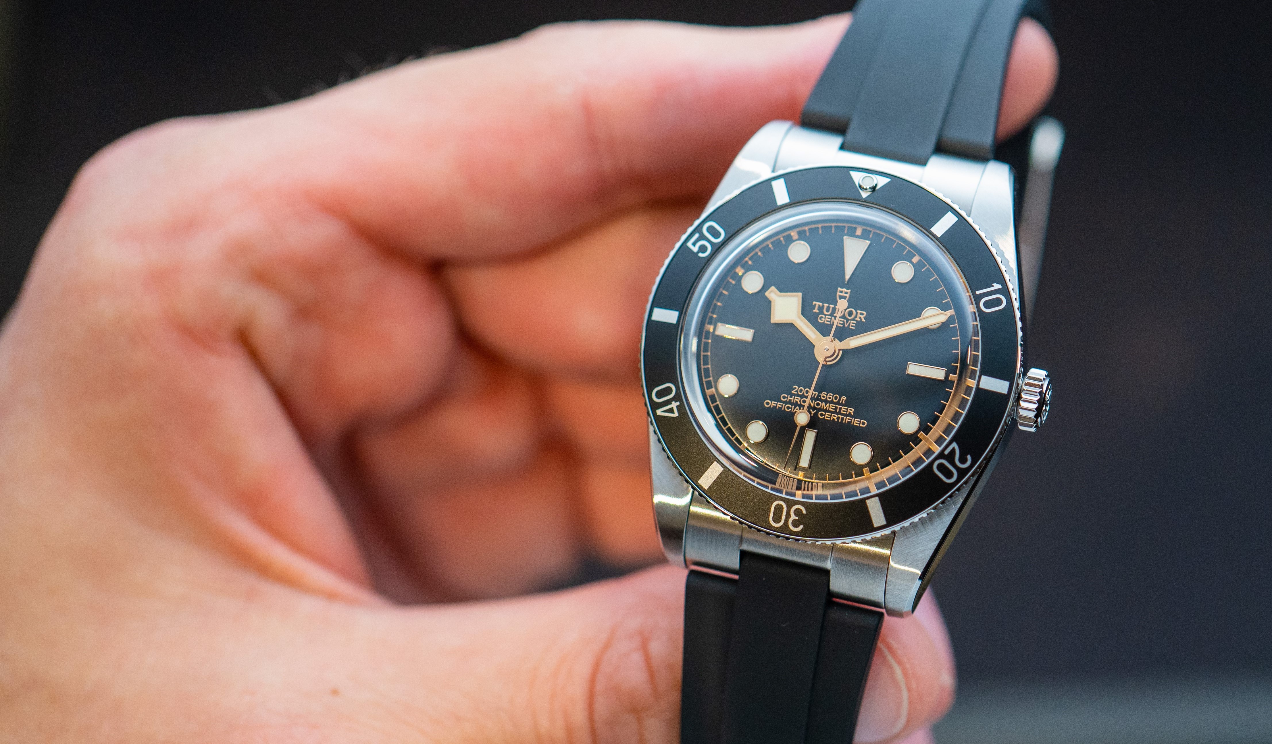 Tudor Black Bay 54 mit schwarzem Kautschukarmband gehalten von einer Hand vor schwarzem Hintergrund