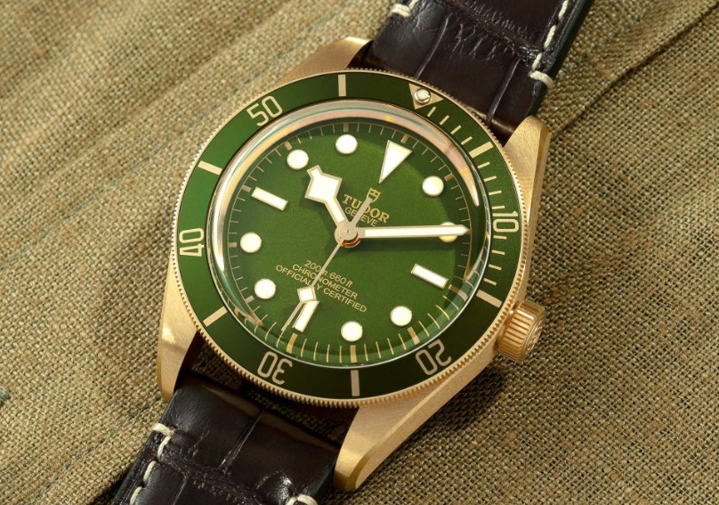 Tudor Black Bay 58 18K mit grünem Zifferblatt und grüner Lünette am braunen Lederarmband liegend auf einem Untergrund aus Holz