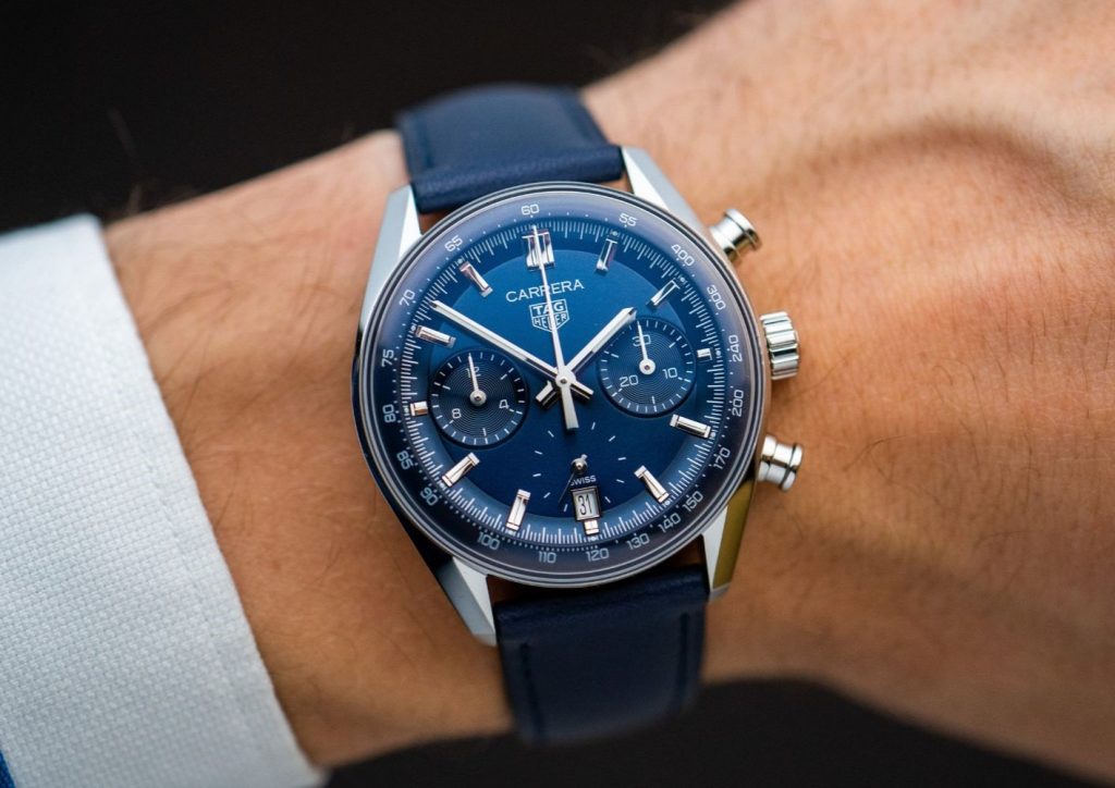 Tag Heuer Carrera Chronograph Glassbox mit blauem Zifferblatt und blauem Armband abgebildet an einem Handgelenk mit weißem Hemdärmel vor dunklem Hintergrund