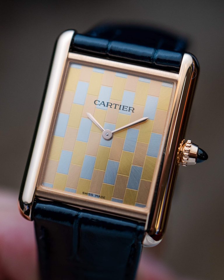 Cartier Tank Louis WGTA0176 mit mehrfarbigem Zifferblatt und an einem schwarzen Lederarmband abgebildet vor dunklem Hintergrund und gehalten von einer Hand