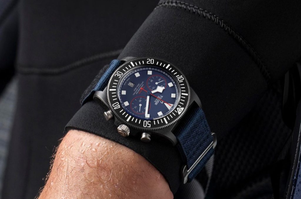 Tudor Pelagos FXD Chronograph mit blauem Zifferblatt und blauem Textilarmband abgebildet an einem Handgelenk mit Tauchanzug