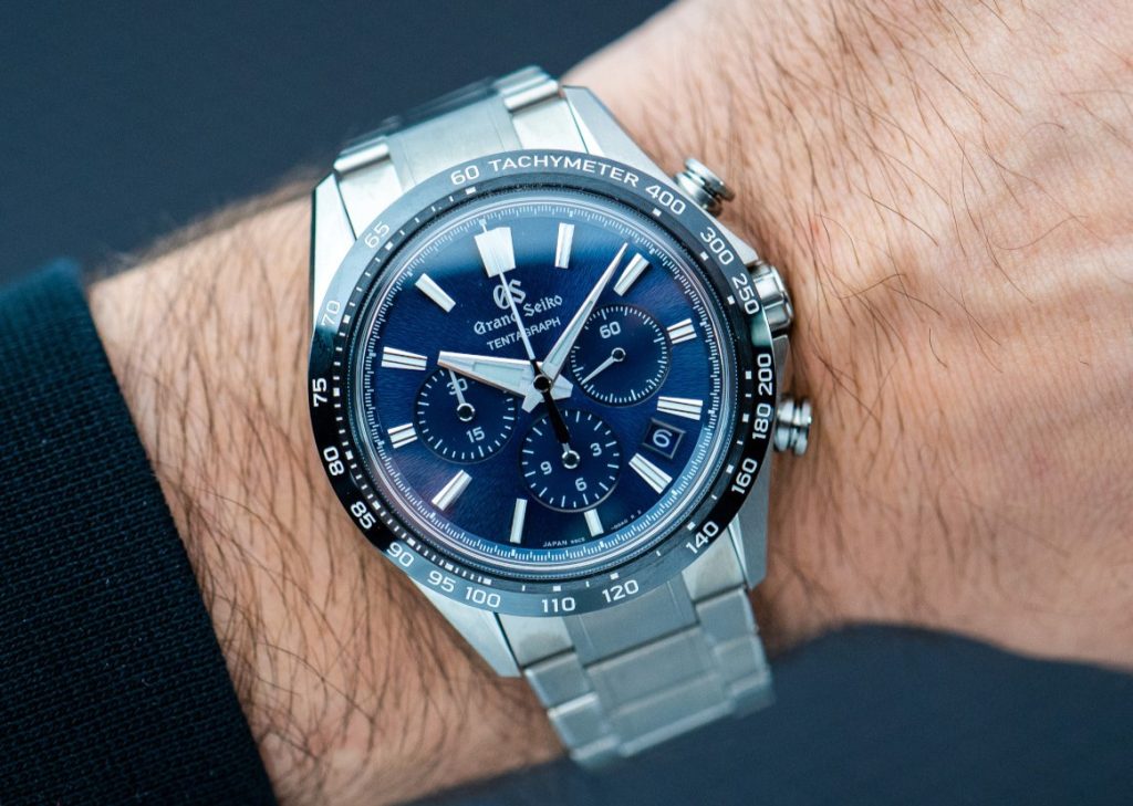 Grand Seiko Tentagraph mit blauem Zifferblatt und schwarzer Lünette am Titanarmband abgebildet an einem Handgelenk vor dunklem Hintergrund