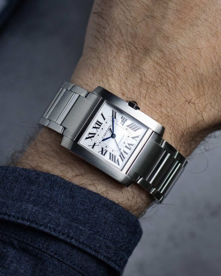 Cartier Tank Française am Edelstahlarmband abgebildet an einem Handgelenk vor grauem Hintergrund