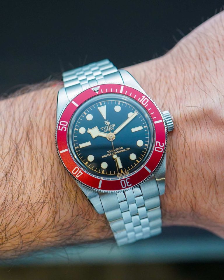 Tudor Black Bay 41 METAS mit roter Lünette und Edelstahlarmband abgebildet an einem Handgelenk vor dunklem Hintergrund