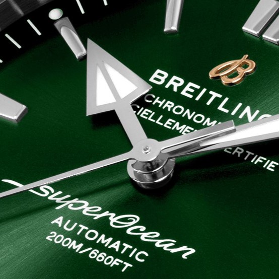 Nahaufnahme des Pfeil-Zeigers der Breitling Superocean Heritage mit grünem Zifferblatt und Breitling-Logo im Hintergrund