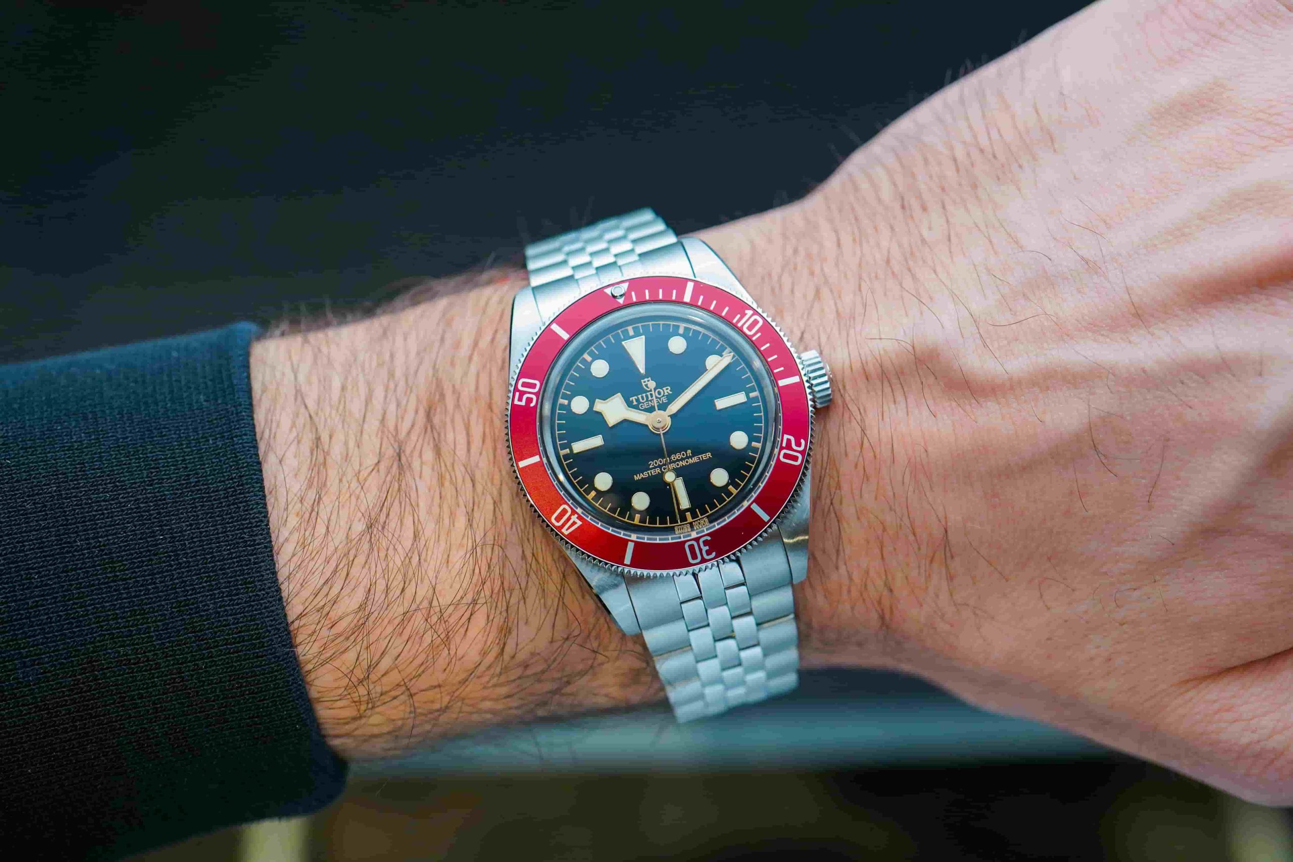 Tudor Black Bay 41 mit roter Lünette und Edelstahlarmband abgebildet an einem Handgelenk mit schwarzem Ärmel