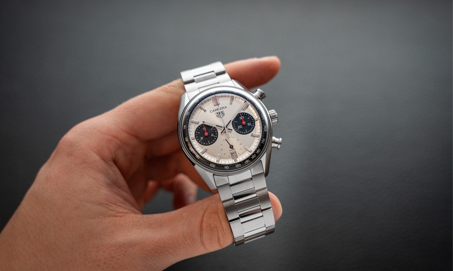 TAG Heuer Carrera Glassbox Panda Chronograph am Stahlband in einer Hand gehalten vor grauem Hintergrund