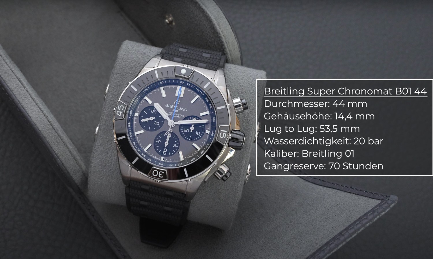 Breitling Super Chronomat B01 Titan am schwarzen Kautschukband um ein Kissen einer Uhrenrolle gebunden vor grauem Hintergrund