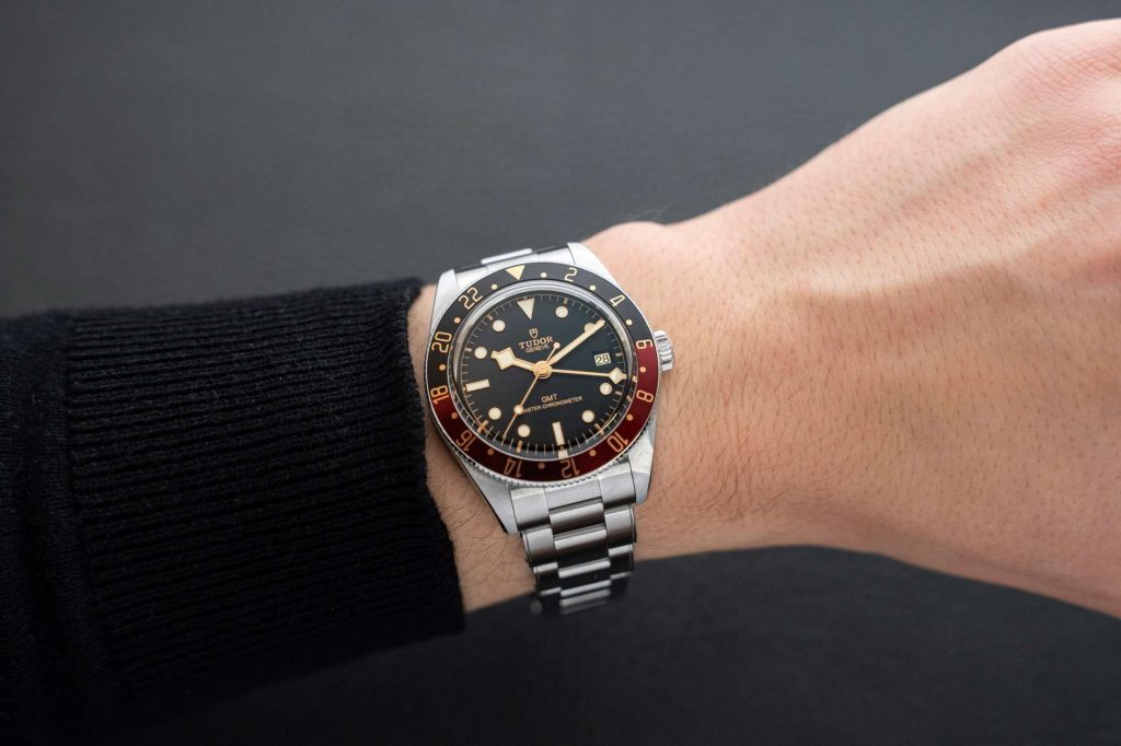 Tudor Black Bay 58 GMT METAS abgebildet an einem Handgelenk mit schwarzem Ärmel vor grauem Hintergrund