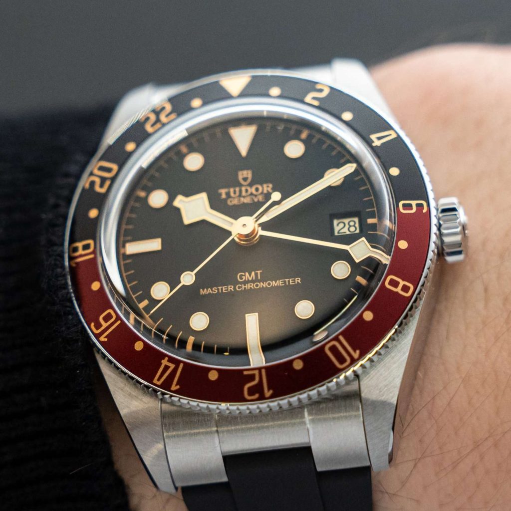 TUDOR Black Bay 58 GMT am schwarzen Kautschukarmband abgebildet an einem Handgelenk mit schwarzem Ärmel vor grauem Hintergrund