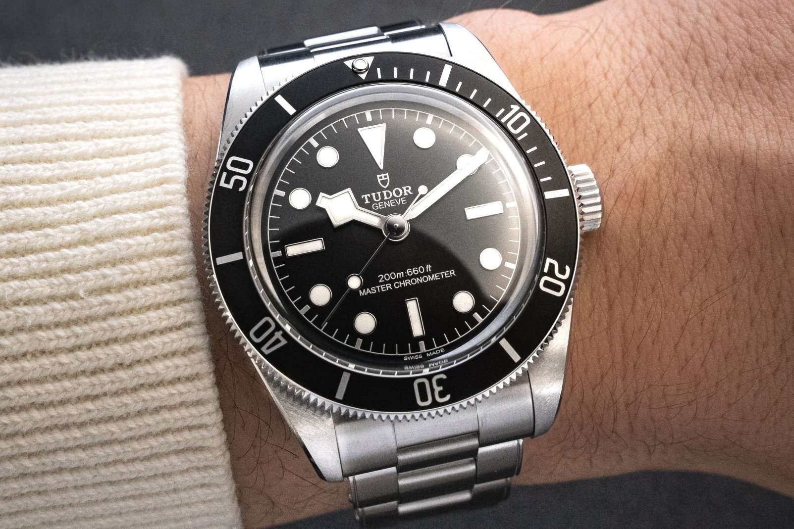 TUDOR Black Bay Monochrome am Edelstahlarmband abgebildet an einem Handgelenk mit weißem Ärmel vor dunklem Hintergrund