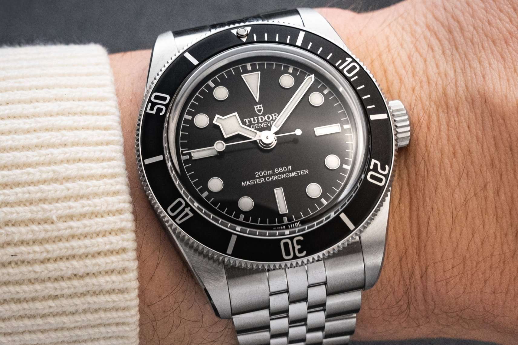 Tudor Black Bay Monochrome am Jubileearmband abgebildet an einem Handgelenk mit weißem Ärmel vor dunklem Hintergrund