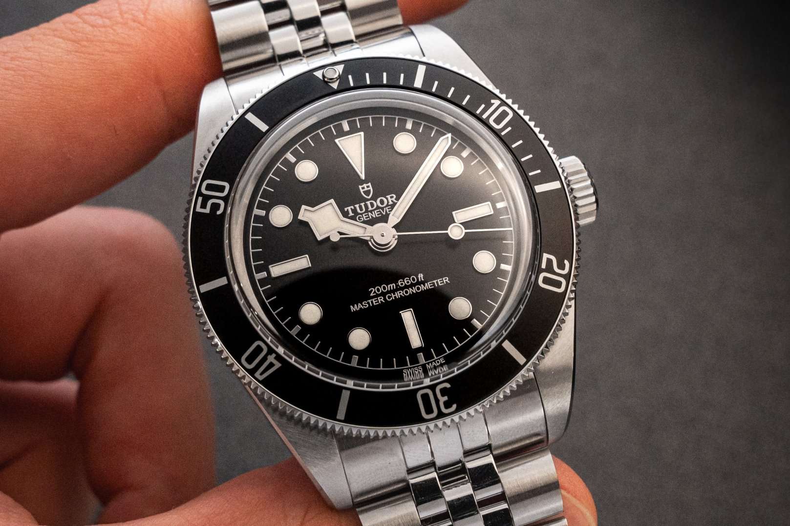 TUDOR Black Bay Monochrome am Jubileearmband gehalten von einer Hand vor dunklem Hintergrund