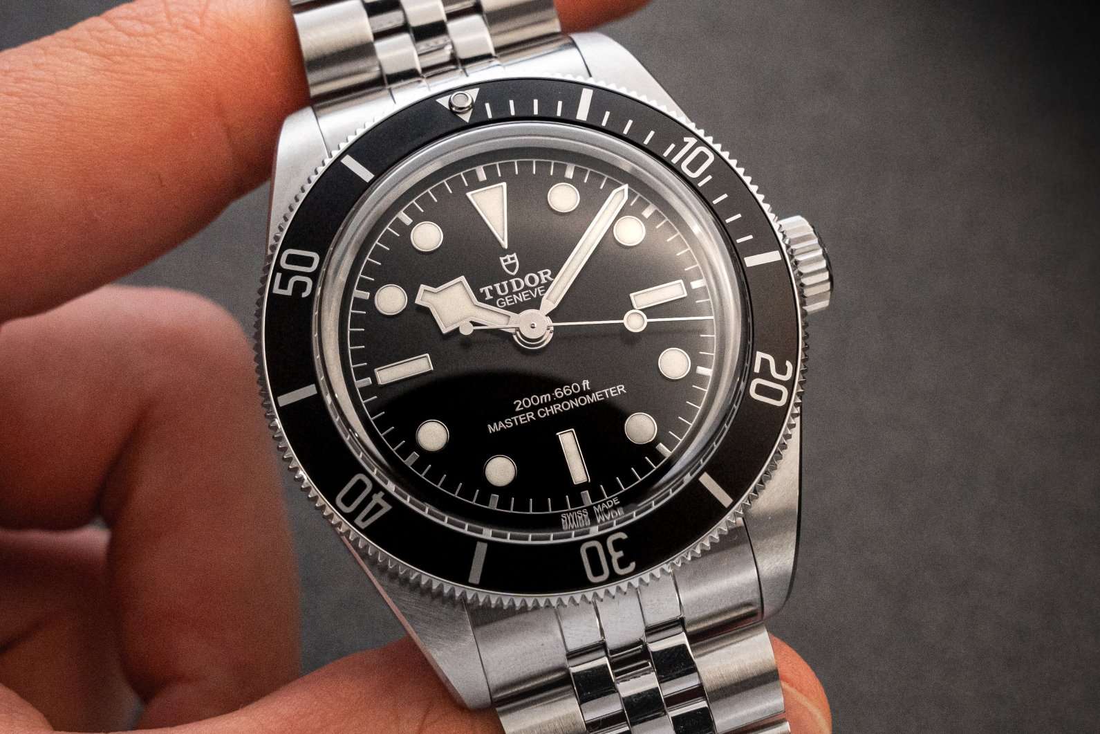 Tudor Black Bay Monochrome am Edelstahlarmband im Jubilee-Stil gehalten von einer Hand vor dunklem Hintergrund