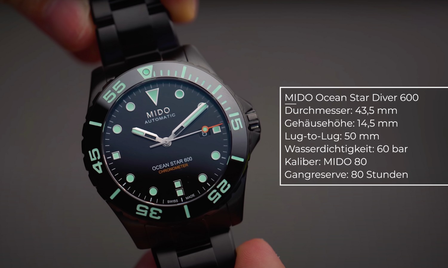 Nahaufnahme der Mido Ocean Star Diver 600 DLC mit schwarzem Zifferblatt, Gehäuse und Armband von zwei Händen gehalten vor grauem Hintergrund