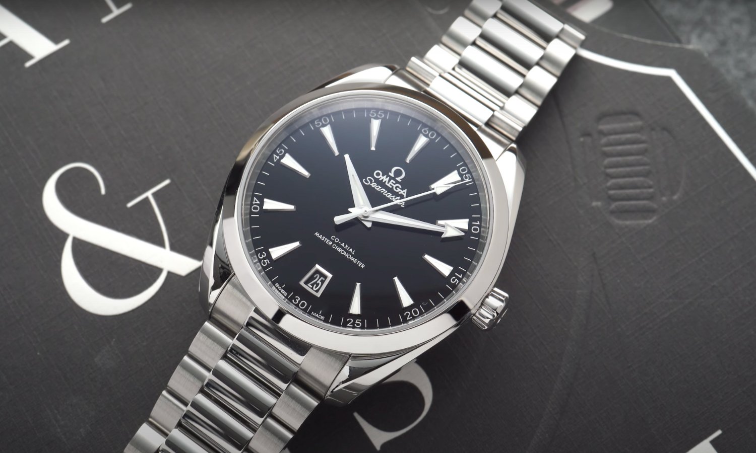 Die OMEGA Seamaster Aqua Terra mit schwarzem Lackzifferblatt am Edelstahlarmband liegend vor schwarzem Hintergrund mit weißer Schrift