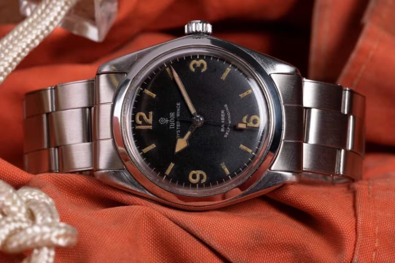 Tudor Oyster Prince Ranger aus 1969 mit schwarzem Zifferblatt am Edelstahlarmband liegend auf einem orangenen Untergrund