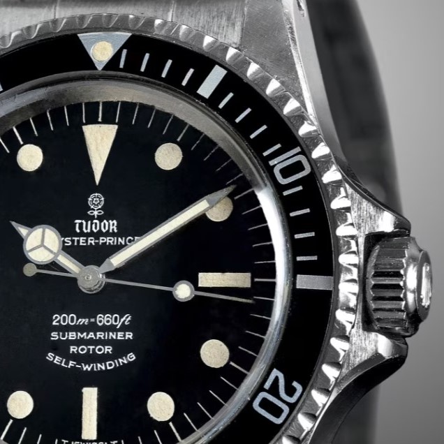 Tudor Submariner Referenz 7928 aus 1967 mit schwarzem Zifferblatt und schwarzer Lünette am Edelstahlarmband vor grauem Hintergrund