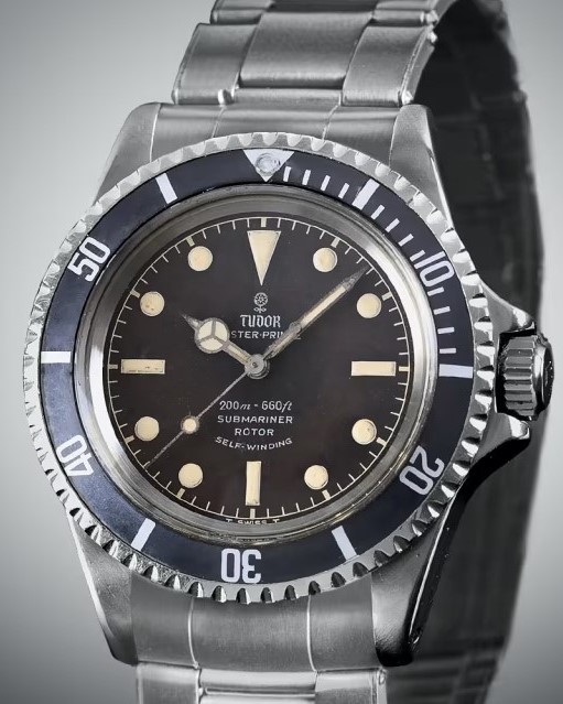 Tudor Submariner aus 1964 mit schwarzem Zifferblatt und schwarzer Lünette am Edelstahlarmband vor grauem Hintergrund