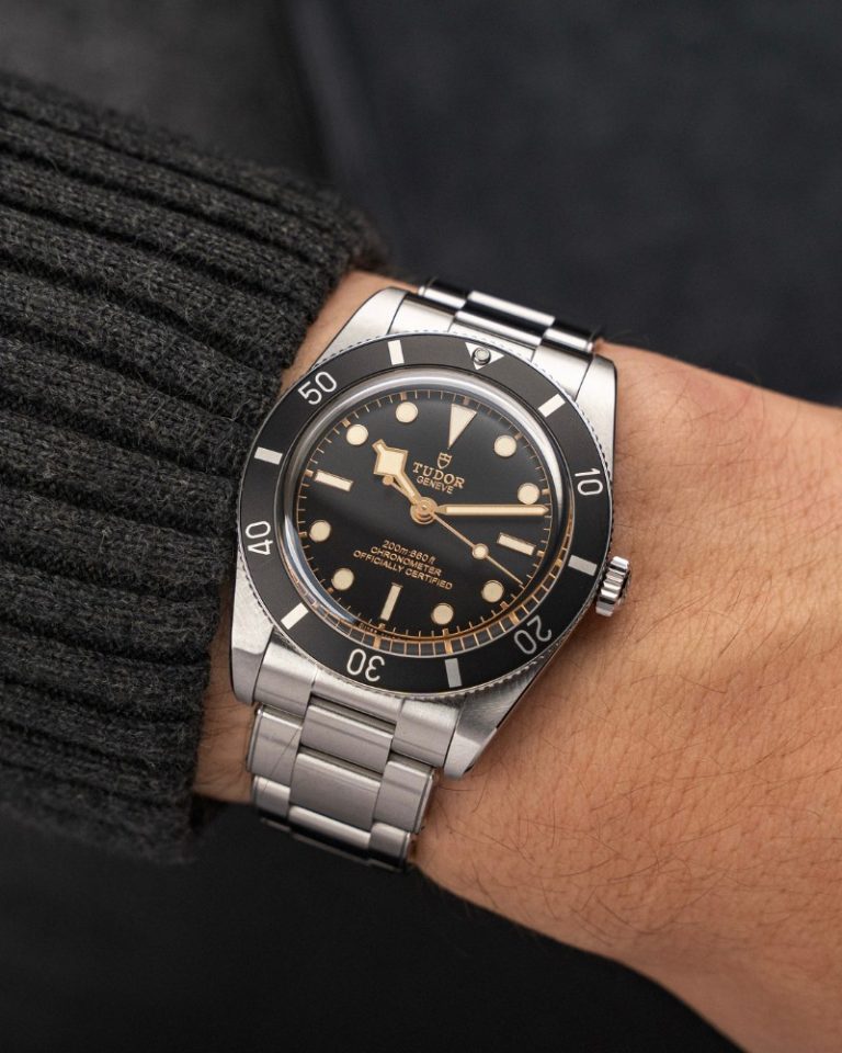 TUDOR Black Bay 54 mit schwarzem Zifferblatt am Edelstahlarmband an einem Handgelenk mit schwarzem Ärmel getragen vor schwarzem Hintergrund