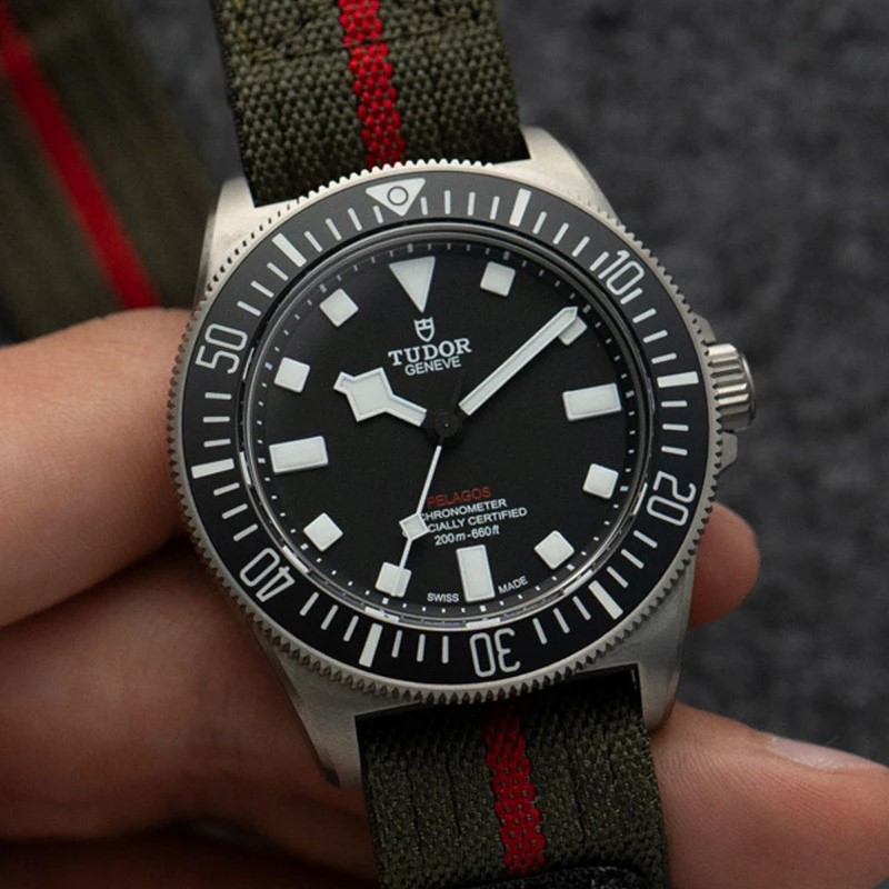 Tudor Pelagos FXD am Textilarmband gehalten von einer Hand vor grauem Hintergrund