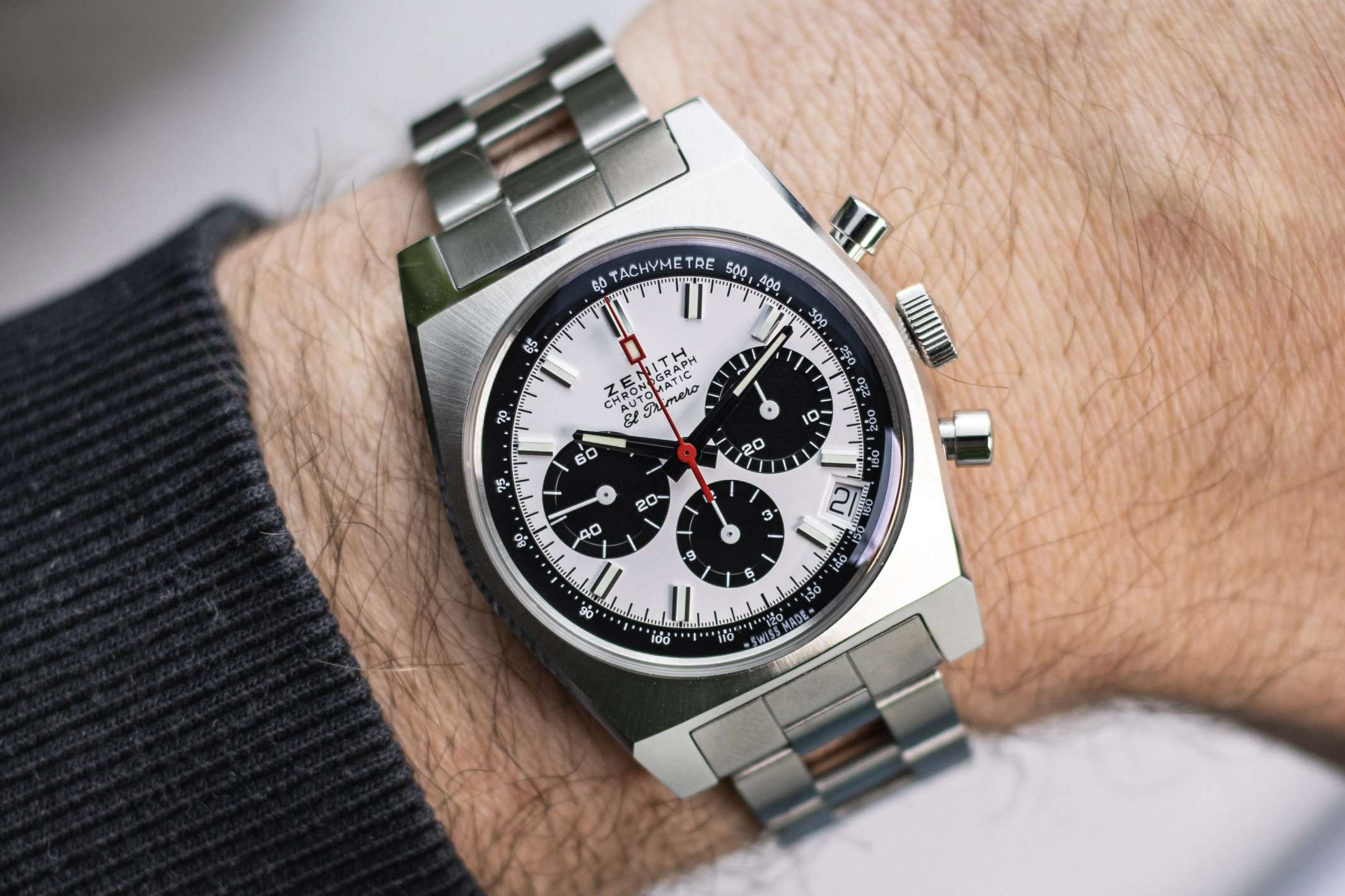 ZENITH Chronomaster Revival El Primero A384 mit weißem Zifferblatt am Edelstahlarmband abgebildet an einem Handgelenk mit schwarzem Ärmel vor hellem Hintergrund