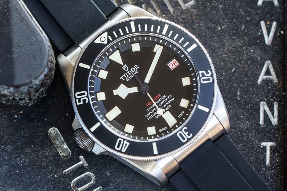 TUDOR Pelagos LHD am Kautschukarmband vor dunklem Hintergrund mit Buchstaben am linken und rechten Bildrand