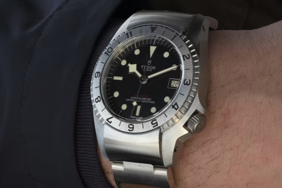 Tudor Black Bay P01 mit Edelstahlarmband abgebildet an einem Handgelenk mit schwarzem Ärmel vor schwarzem Hintergrund