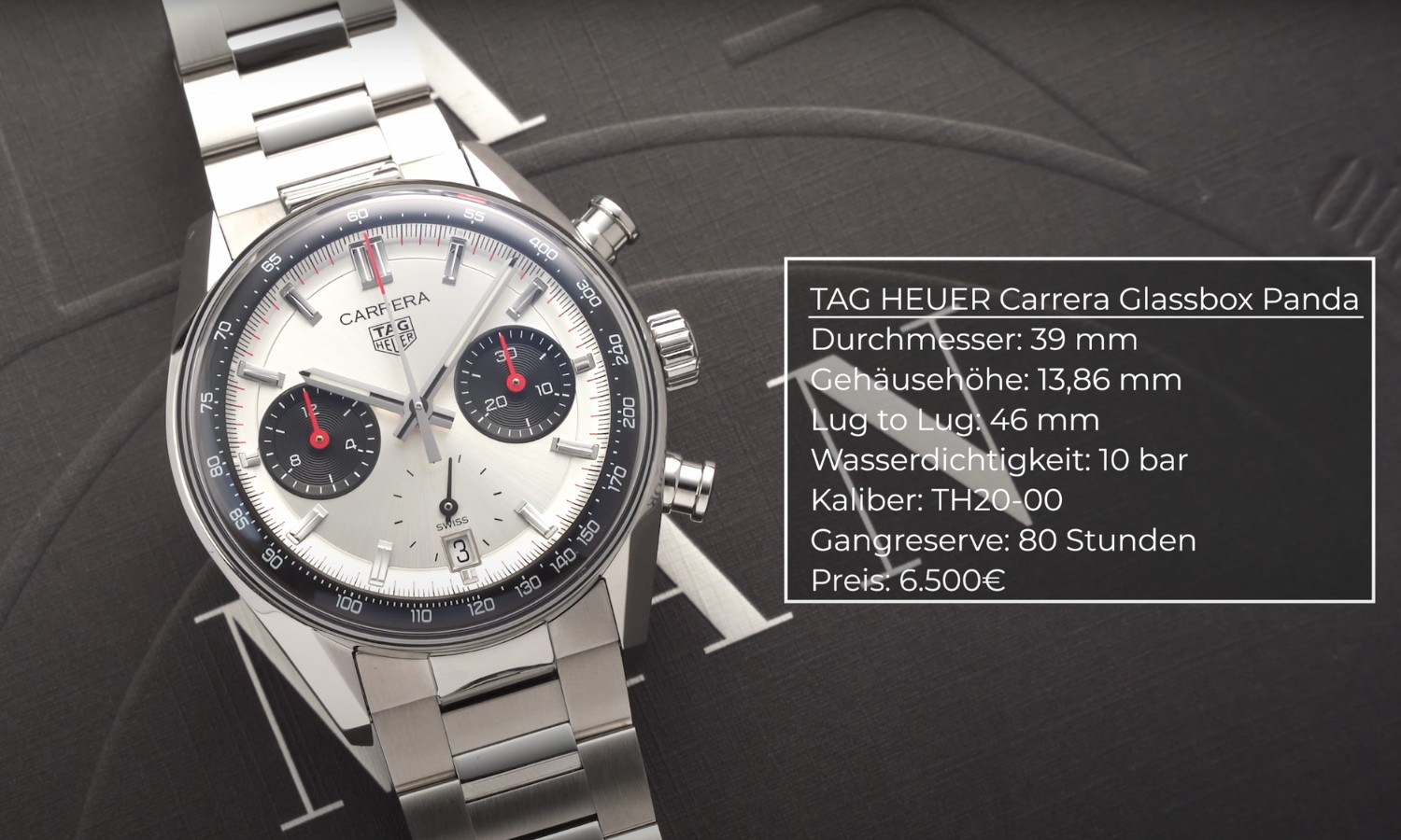 Der TAG Heuer Carrera Glassbox Panda Chronograph mit silbernem Zifferblatt am Edelstahlarmband liegend vor dunkelgrauem Hintergrund mit weißer Schrift