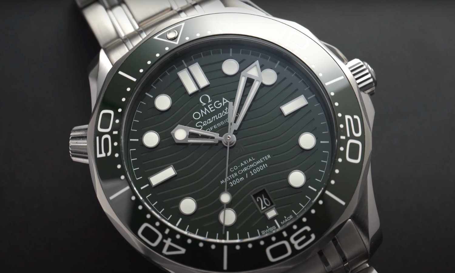 Nahaufnahme des Zifferblatts der OMEGA Seamaster Diver 300M mit grünem Zifferblatt vor schwarzem Hintergrund