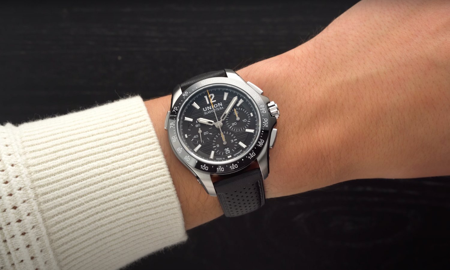 Die UNION Glashütte Belisar Chronograph Sport mit schwarzem Zifferblatt am schwarzen Lederarmband an einem Handgelenk mit beigem Ärmel