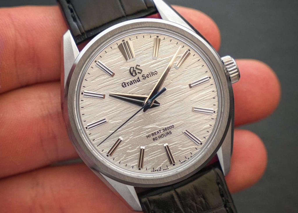 Nahaufnahme des weißen Zifferblattes der Grand Seiko SLGW003, das einer Birkenstruktur nachempfunden ist. Gehalten wird die Uhr von einer Hand