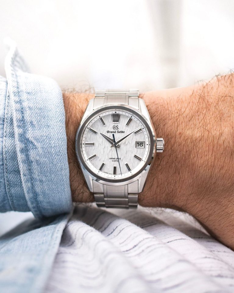 Die Grand Seiko White Birch am Edelstahlarmband an einem Handgelenk mit hellblauem Ärmel vor hellem Hintergrund