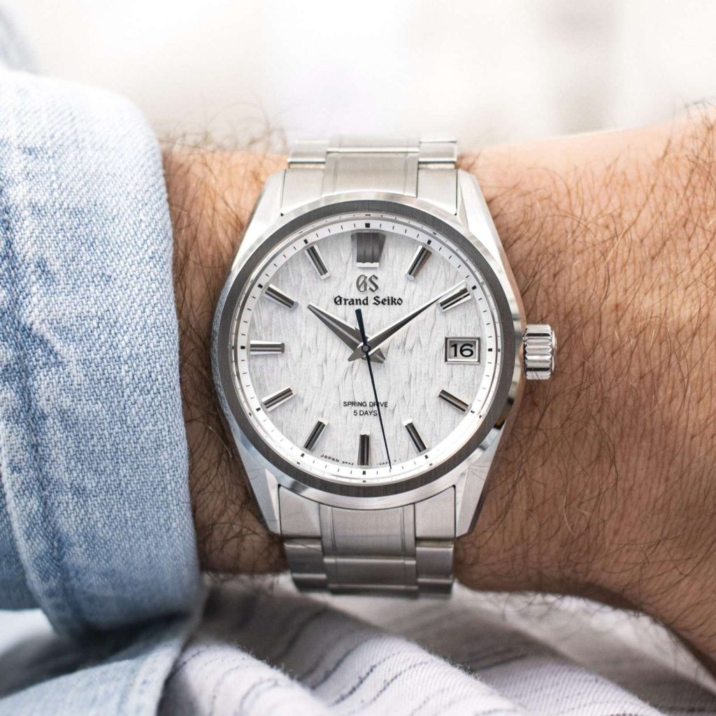 Grand Seiko White Birch abgebildet an einem Handgelenk mit hellblauem Ärmel vor hellem Hintergrund