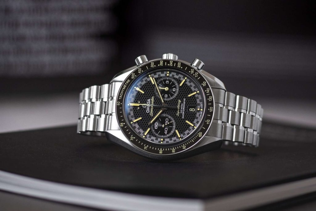 Omega Speedmaster Super Racing liegend auf einem schwarzen Buch vor dunklem Hintergrund mit weißer Schrift