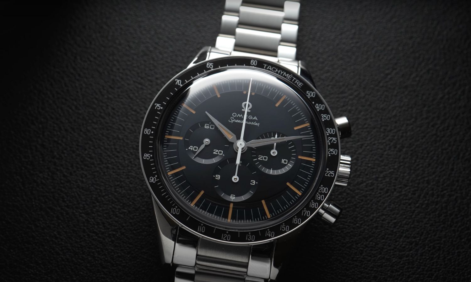 Die OMEGA Speedmaster First OMEGA in Space mit dunkelblauem Zifferblatt am Edelstahlarmband liegend vor schwarzem Hintergrund