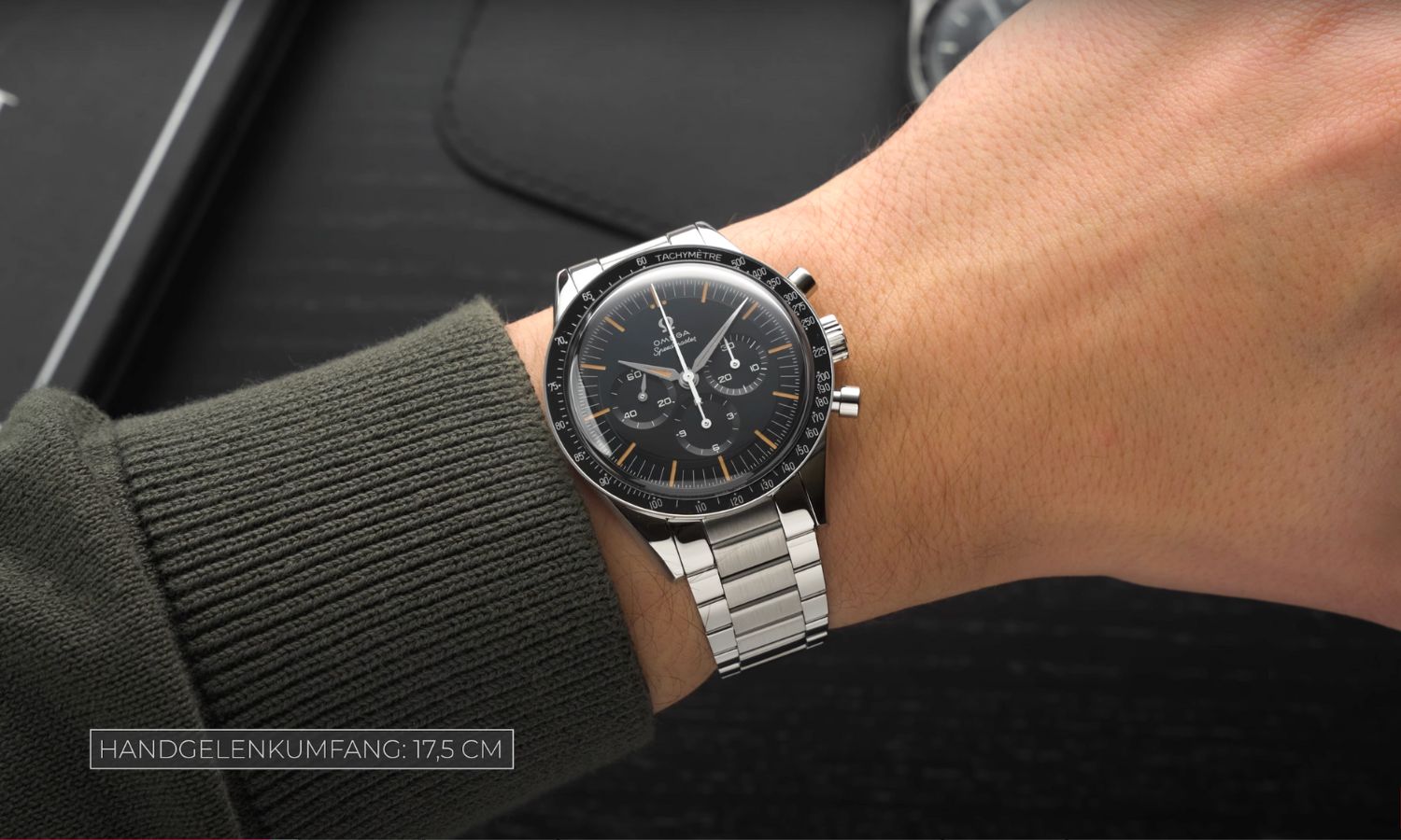 Die OMEGA Speedmaster First OMEGA in Space mit dunkelblauem Zifferblatt am Edelstahlarmband an einem Handgelenk getragen vor schwarzem Hintergrund