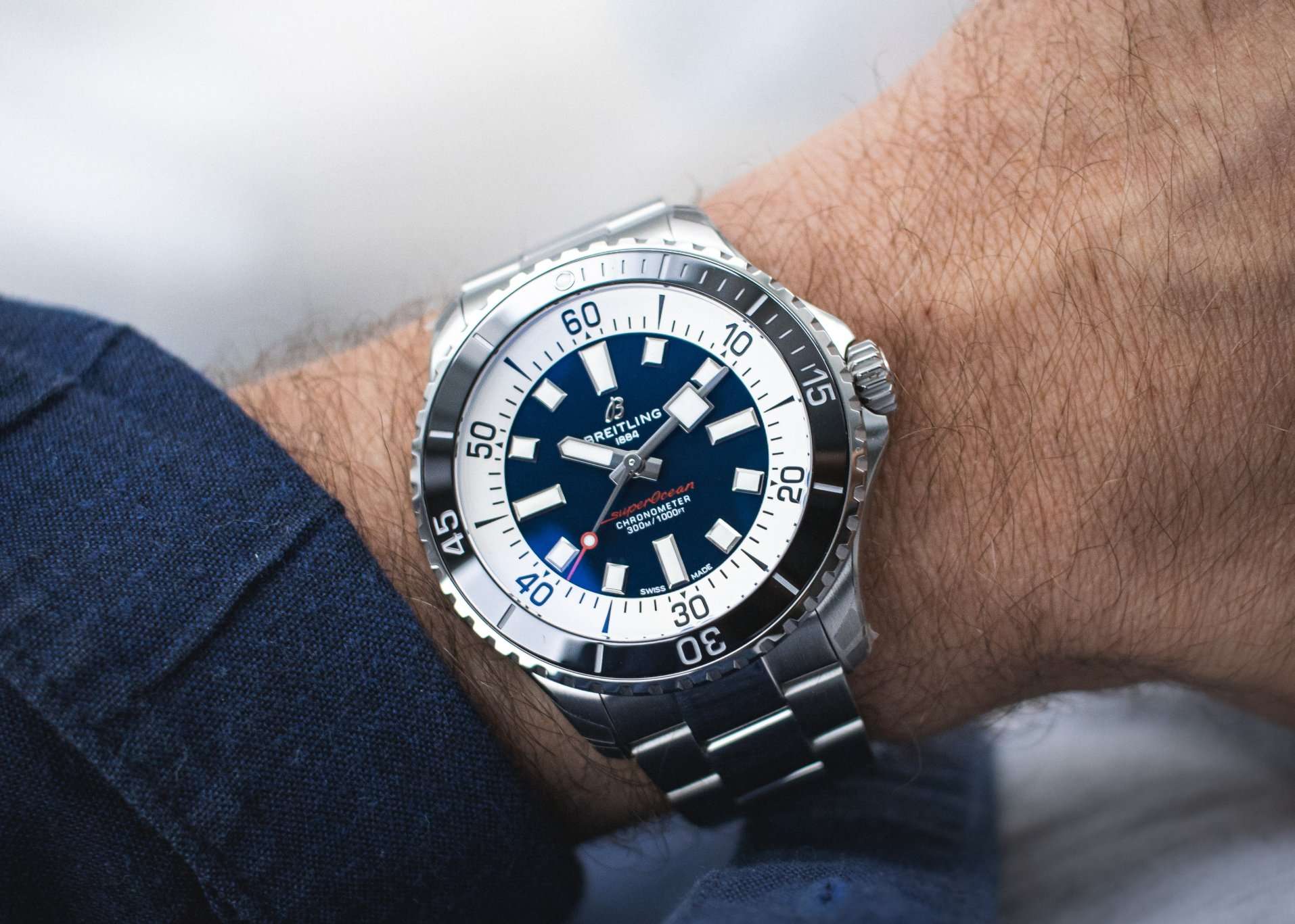 Die Breitling Superocean mit blauem Zifferblatt und schwarzer Lünette mit Edelstahlarmband abgebildet an einem Handgelenk vor hellem Hintergrund