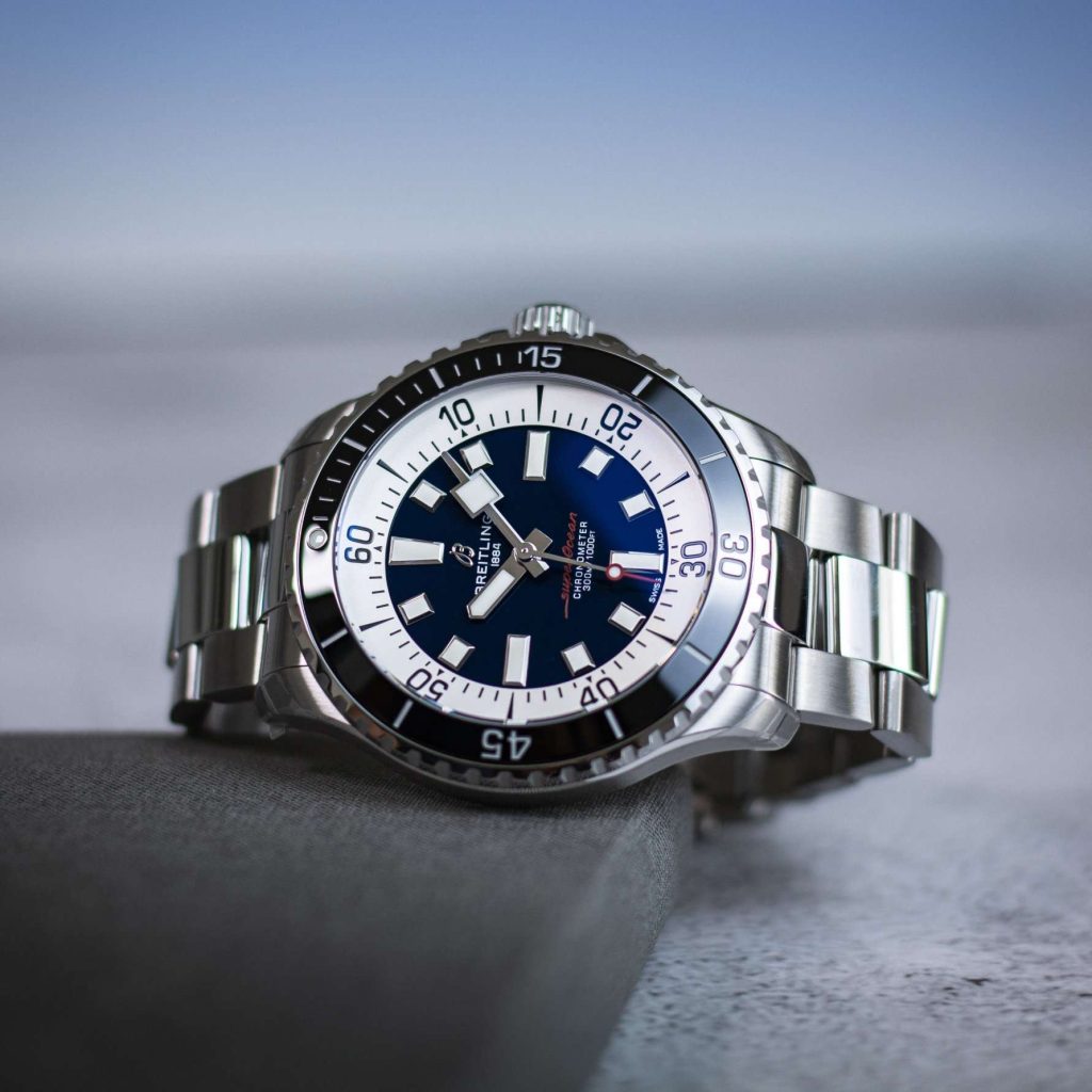 Breitling Superocean Automatic 44 mit blauem Zifferblatt und schwarzer Lünette abgebildet am Edelstahlarmband vor hellem Hintergrund liegend auf einer schwarzen Kante