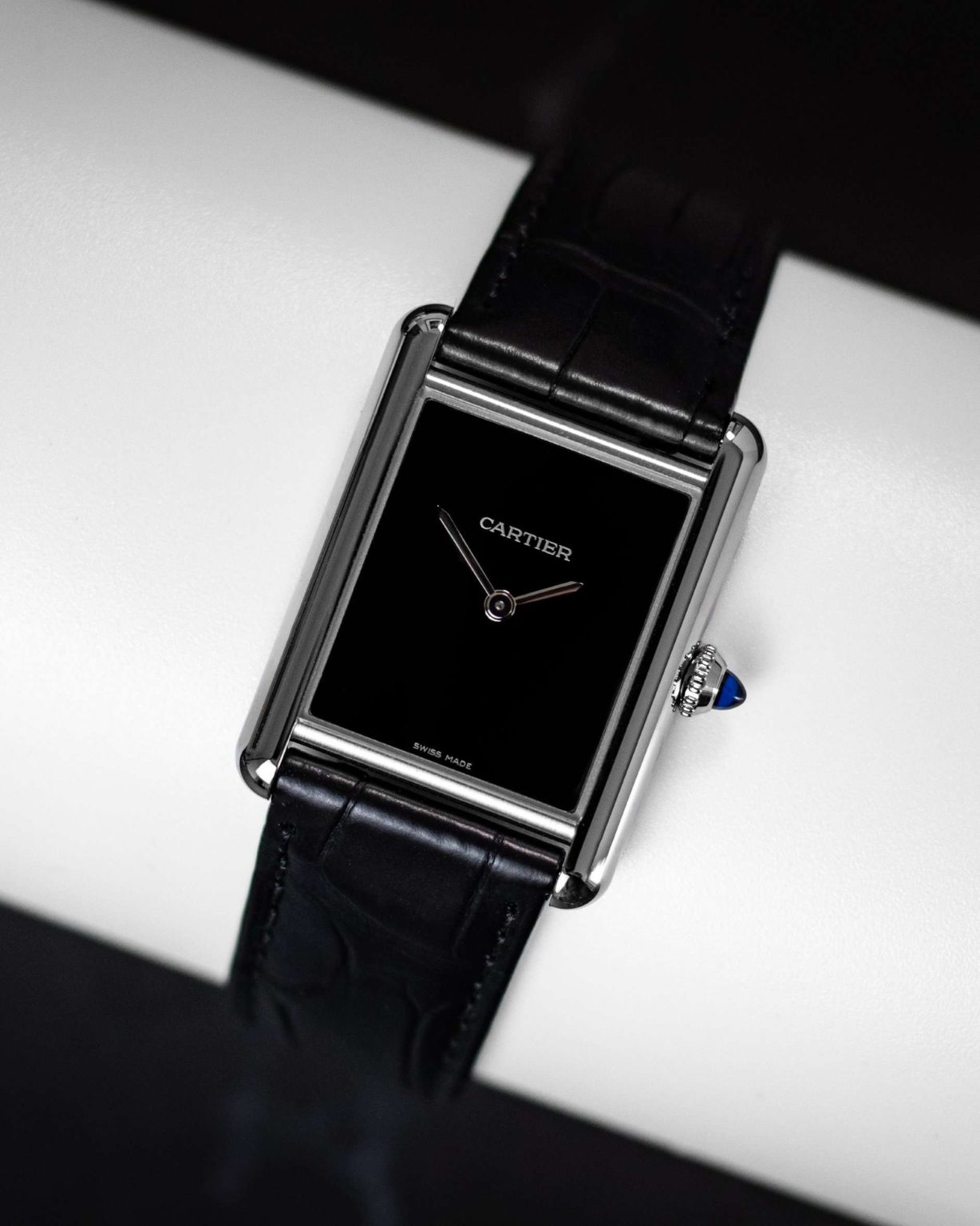 Cartier Tank Must mit schwarzem Zifferblatt und schwarzem Lederarmband vor schwarzweißem Hintergrund